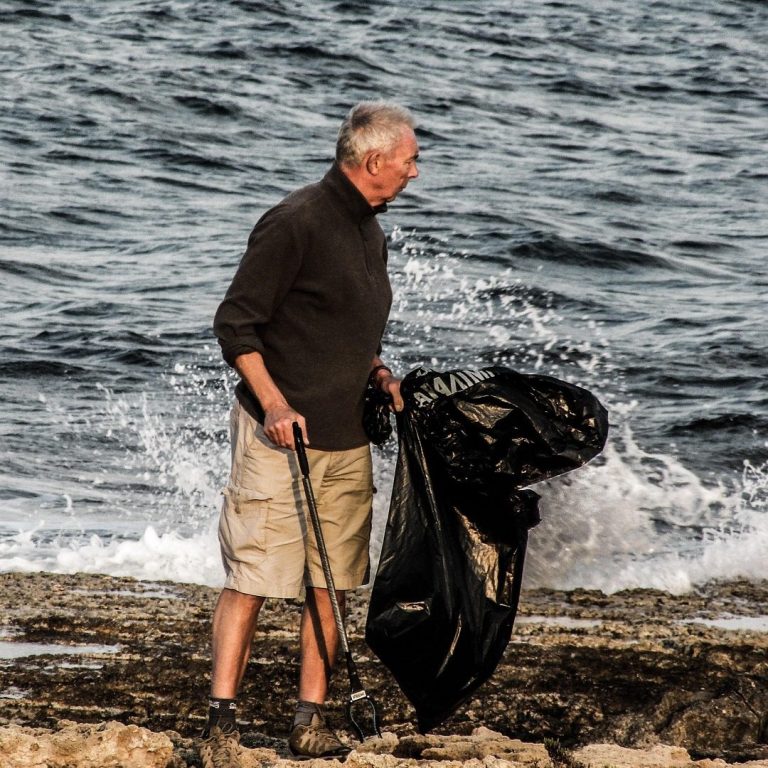 Volunteer Vacation Man in shorts cleaning up trash on a rocky shore near the water.