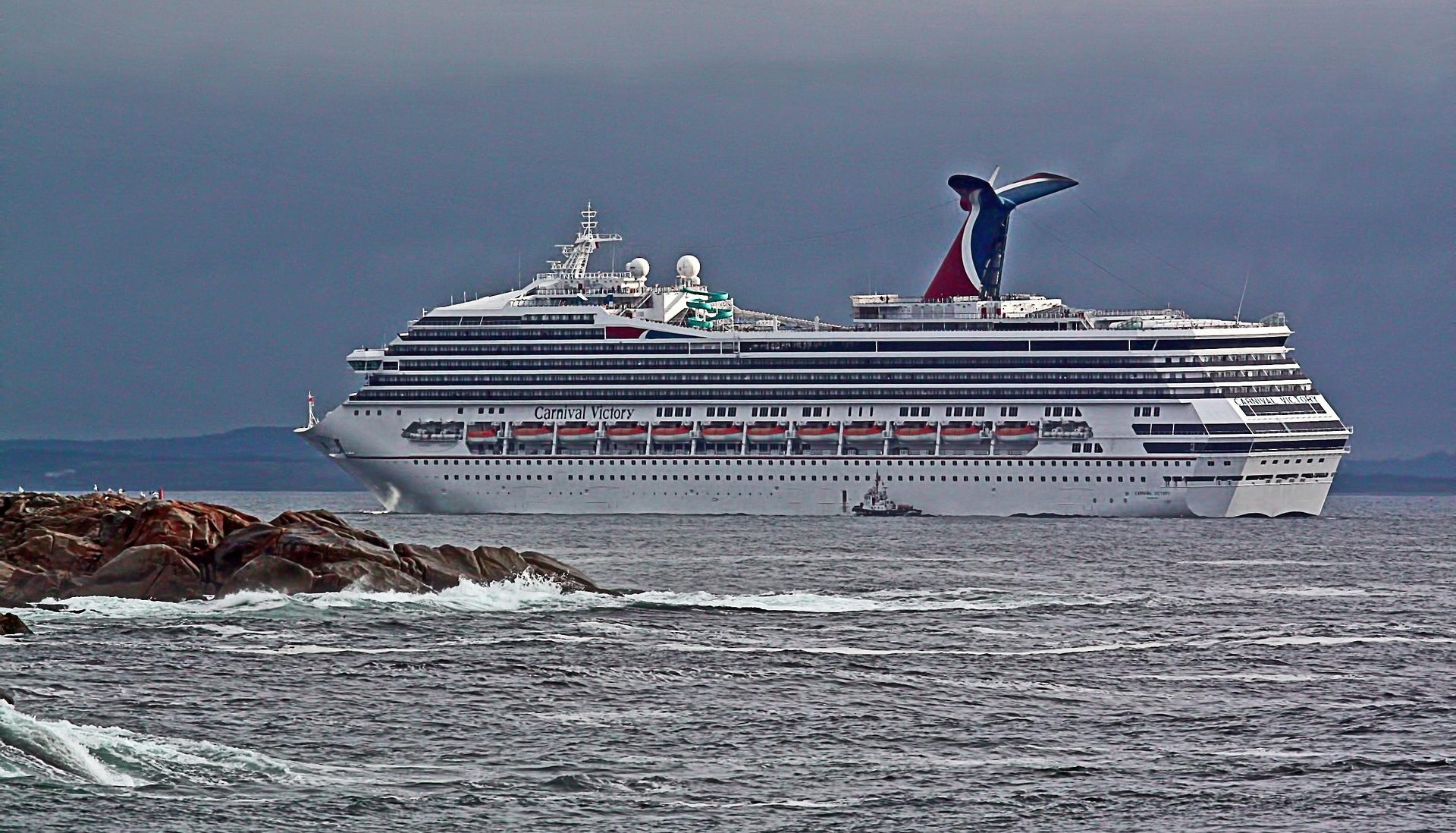 Dream Carnival Elation A large cruise ship with a red and blue funnel sails near rocky shores.