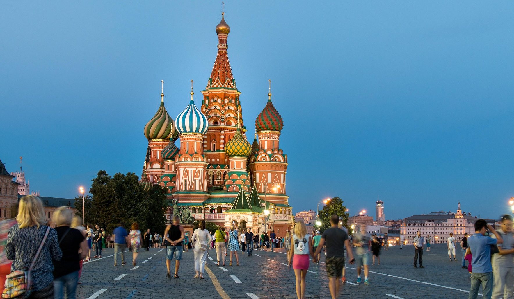 Personal Travel Assistant St. Basil's Cathedral at dusk, with colorful domes and people walking in the foreground.