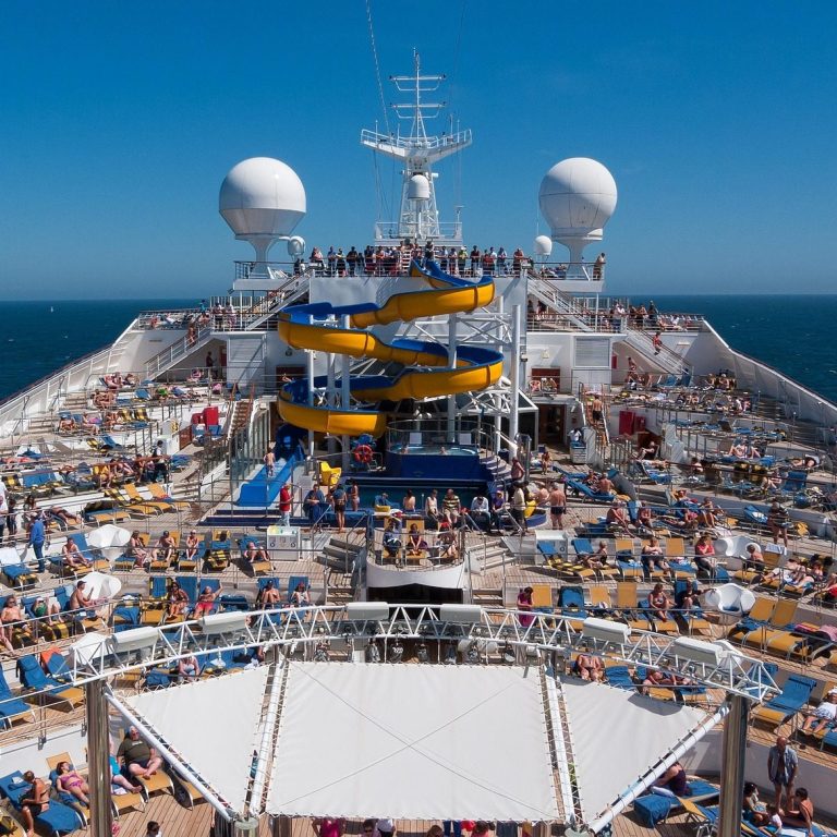 Cruise Vacation Crowded cruise ship deck with yellow water slides and numerous sun loungers under clear blue sky.