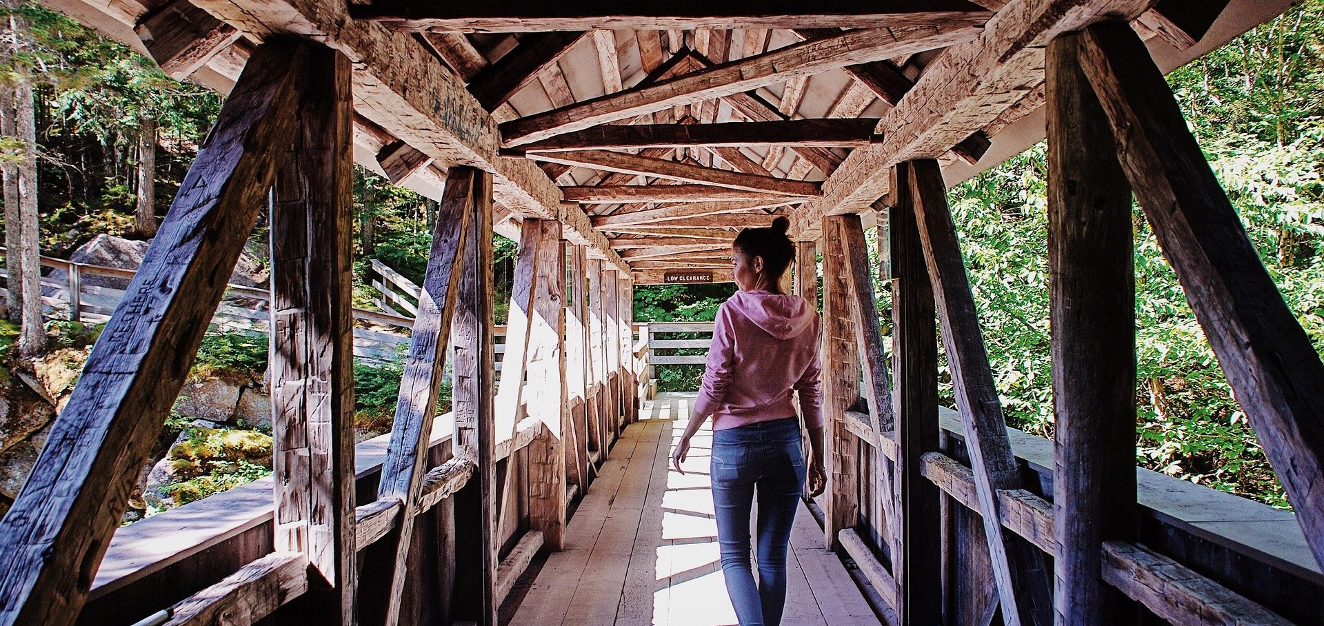 Travel With Car Hire Person walking through a wooden bridge surrounded by greenery.