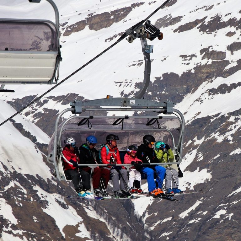 Ski & Snow Vacation Skiers riding a lift over snowy mountains.