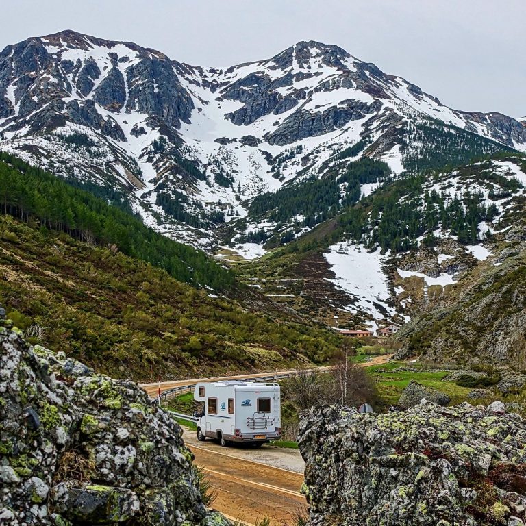 Road Trip Vacation RV on a winding road in a mountainous landscape with snow-capped peaks.