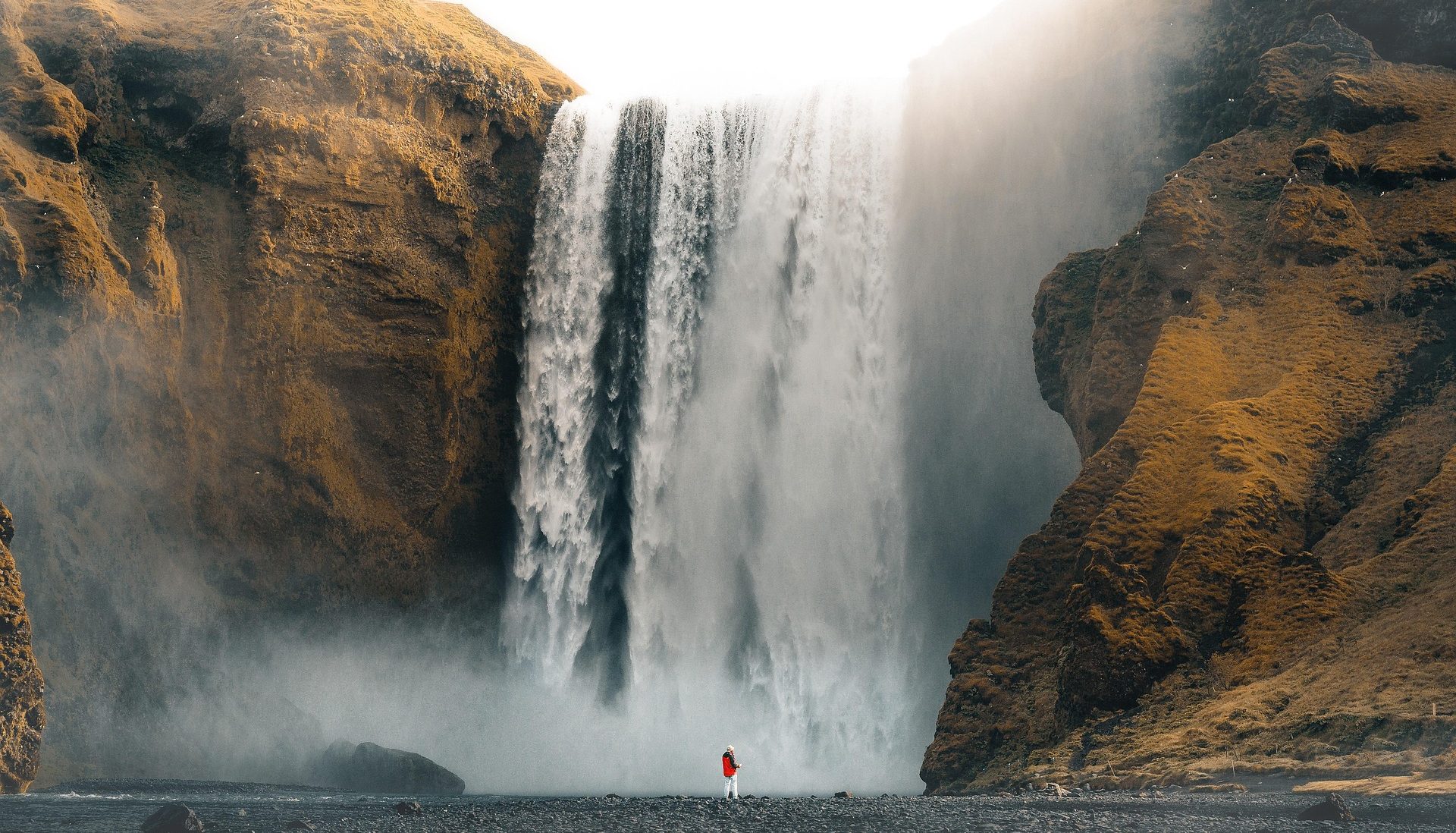 Award-Winning Travel Advisor A majestic waterfall cascading down rocky cliffs, with a person in red at the base.