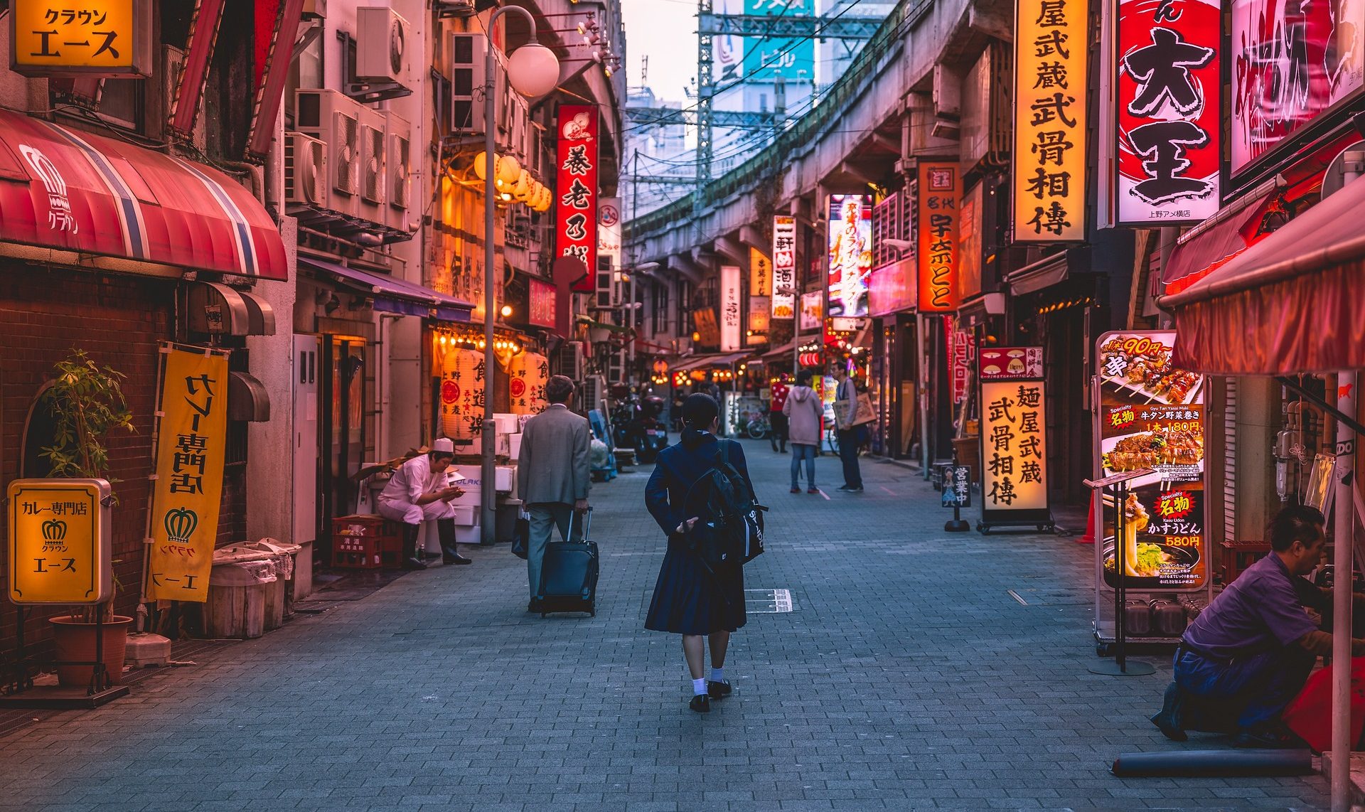 corporate travel coordinator A vibrant street scene with neon signs and a person walking in a city alley.