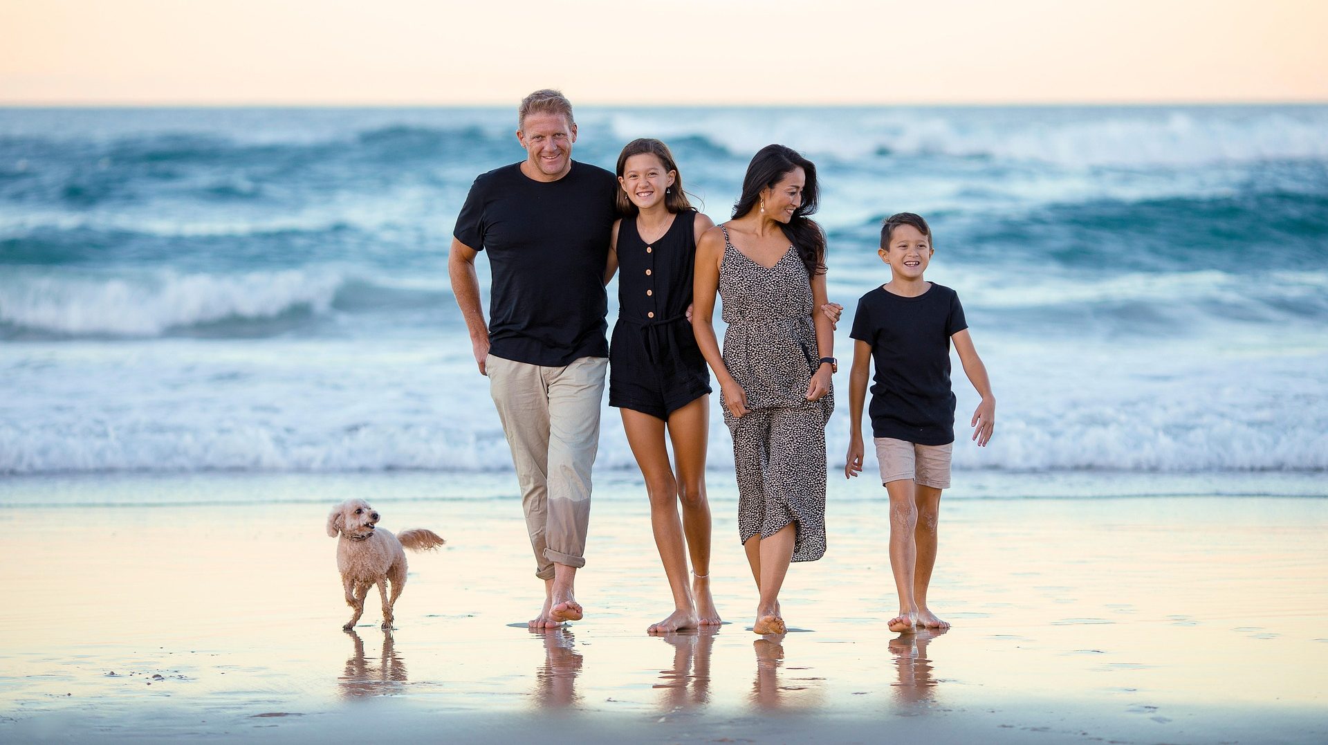 Luxury Agents Family walking along the beach with a dog, waves in the background during sunset.