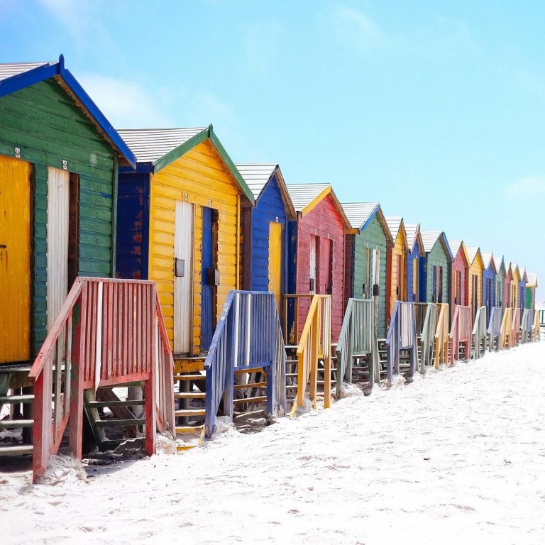 Beach Vacation Colorful beach huts lined up on a sandy shore under a blue sky.